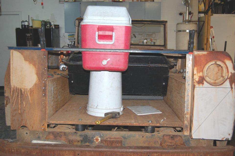 Rear view into rusty Scout bed with plywood floor, tailgate removed, cooler on a bucket
