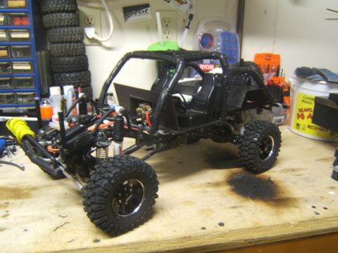 1988 Ford Bronco - A custom RC crawler chassis with off-road tires and a roll cage sits on a workbench, surrounded by tools and spare parts.