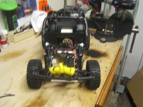 1988 Ford Bronco - RC crawler chassis with yellow winch and exposed mechanical components on a wooden surface.