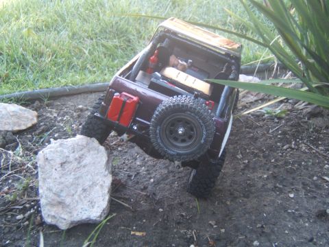 1988 Ford Bronco - This RC crawler is navigating a rocky outdoor terrain, with grass and plants in the background.