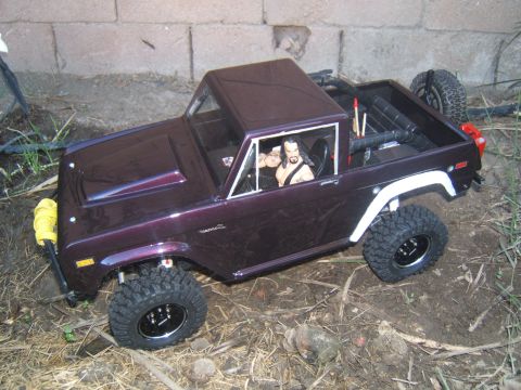 1988 Ford Bronco - A purple RC crawler with a driver figure is positioned on uneven terrain.
