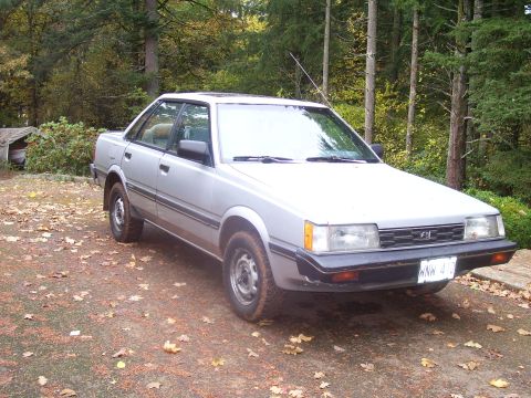 1991 Ford Bronco - Silver Subaru sedan parked outdoors on a dirt road covered with fallen leaves.
