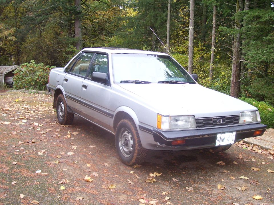 Silver Subaru sedan parked on a dirt road with autumn leaves on the ground. License plate reads 'NNW 417'