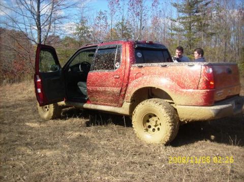 2002 Ford Sport Trac - A muddy red 2002 Ford Sport Trac with its driver's door open sits in a field after off-roading.
