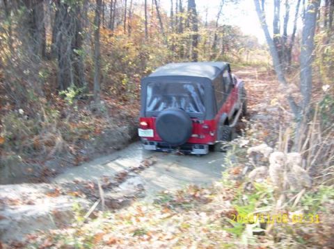 2002 Ford Sport Trac - A red Jeep Wrangler navigates a muddy path through a wooded area during autumn.