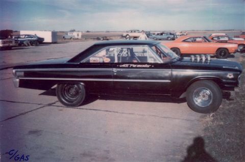 1963 Ford Galaxie - A black 1963 Ford Galaxie drag car is parked on asphalt with other vehicles in the background.