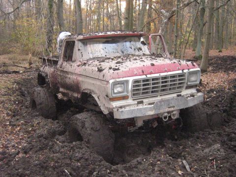 1990 Ford Bronco - This heavily modified Ford pickup truck is deeply embedded in thick mud and appears to be stuck in a wooded area.