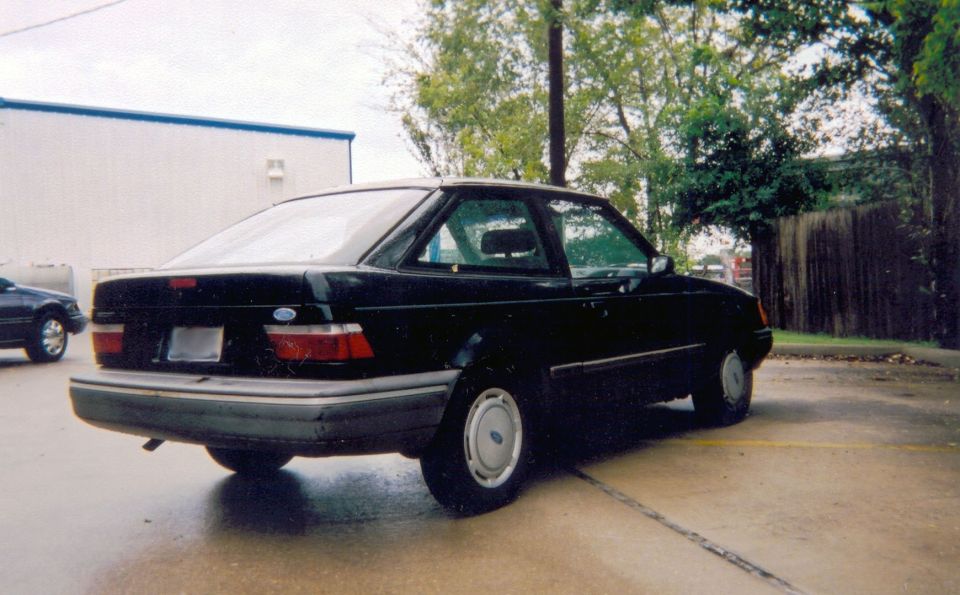 Black late-80s Ford Escort two-door, rear three-quarter view