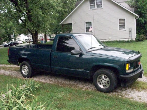 Dark green 1995 GMC Sierra 1500 pickup truck parked on gravel in front of a house