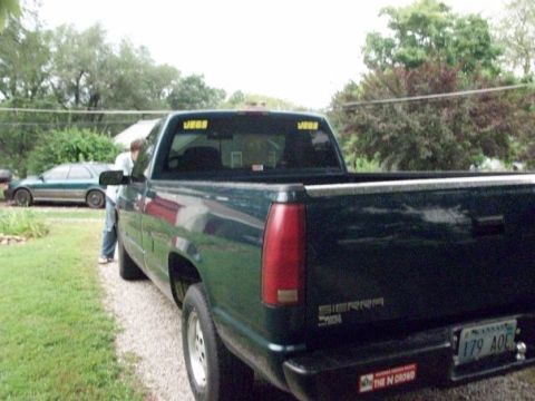 1995 GMC Sierra 1500 - A dark green pickup truck is parked on a gravel driveway with a person standing by the driver's side door.