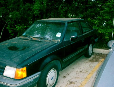 1989 Ford Escort - This 1989 Ford Escort coupe is seen parked in a lot with trees in the background.