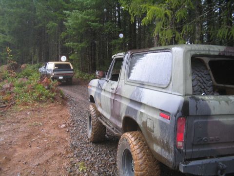 1989 Ford Bronco - Two Ford Broncos drive down a wooded gravel road in the rain.