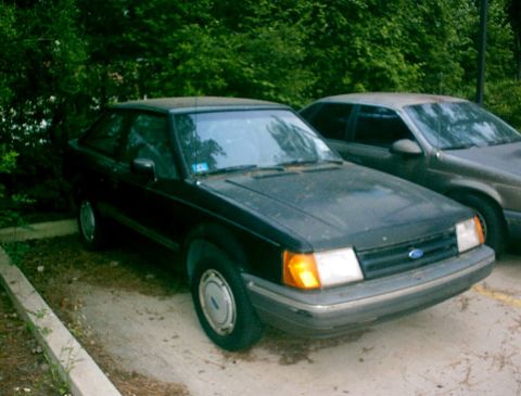 1989 Ford Escort - A black 1989 Ford Escort is parked outside next to another vehicle.
