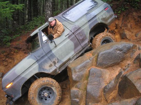 1989 Ford Bronco - A driver navigates a camouflaged 1978 Ford Bronco over a challenging rocky obstacle.