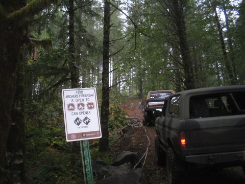 1989 Ford Bronco - Off-road vehicles navigate a trail in a wooded area, with a sign indicating trail information.