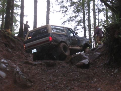 1989 Ford Bronco - A 1989 Ford Bronco navigates a challenging rocky path through a dense forest.