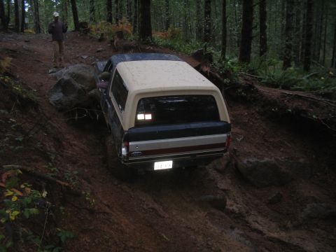 1989 Ford Bronco - Ford Bronco navigates a challenging, wet, and rocky off-road trail in a dense forest.