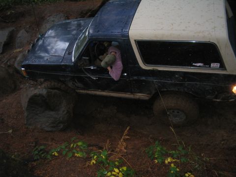 1989 Ford Bronco - This vehicle is navigating a challenging off-road course with large rocks and mud.