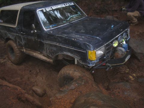 1989 Ford Bronco - A Ford Bronco navigates a challenging muddy terrain, with one wheel deep in the mire.
