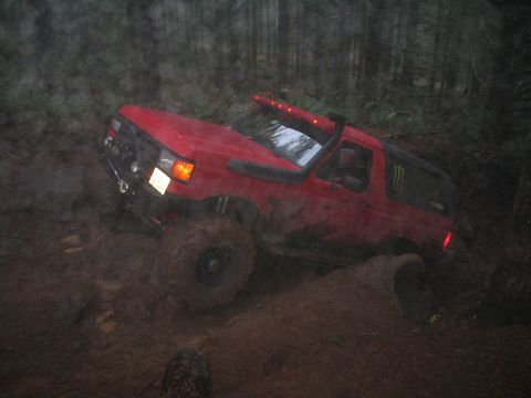 1989 Ford Bronco - Red 1989 Ford Bronco struggling through deep mud on a forest trail.