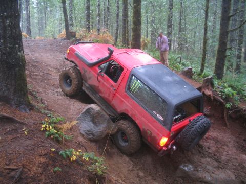 1989 Ford Bronco - A red 1989 Ford Bronco navigates a challenging, muddy off-road course in a forest.