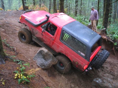 1989 Ford Bronco - This red Ford Bronco navigates a challenging off-road trail, demonstrating its capabilities on rough terrain.