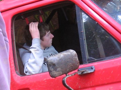 1989 Ford Bronco - Close-up of a person inside a red vehicle, with a muddy side mirror in the foreground.