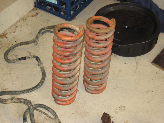 Pair of worn orange coil springs standing on a concrete garage floor