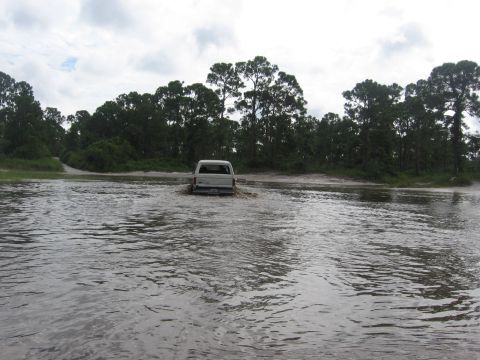 1989 Ford Bronco - A 1989 Ford Bronco navigates through flooded terrain under a cloudy sky.