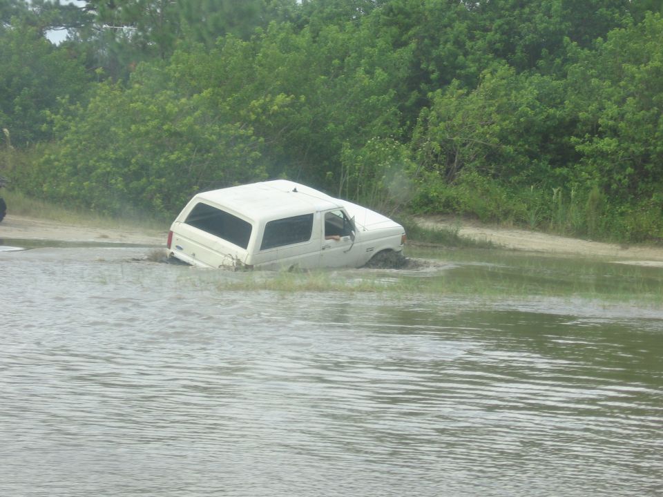 White 1989 Ford Bronco stuck in mud and water