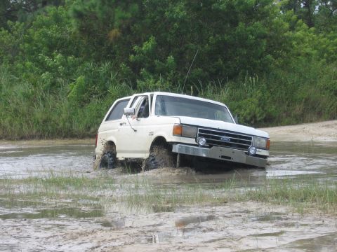 1989 Ford Bronco - White Ford Bronco navigating a muddy off-road course.