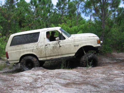 1989 Ford Bronco - This lifted 1989 Ford Bronco navigates a muddy trail with large off-road tires.