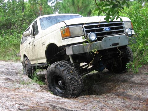 1989 Ford Bronco - A white Ford Bronco is stuck in the mud, viewed from the front-left.