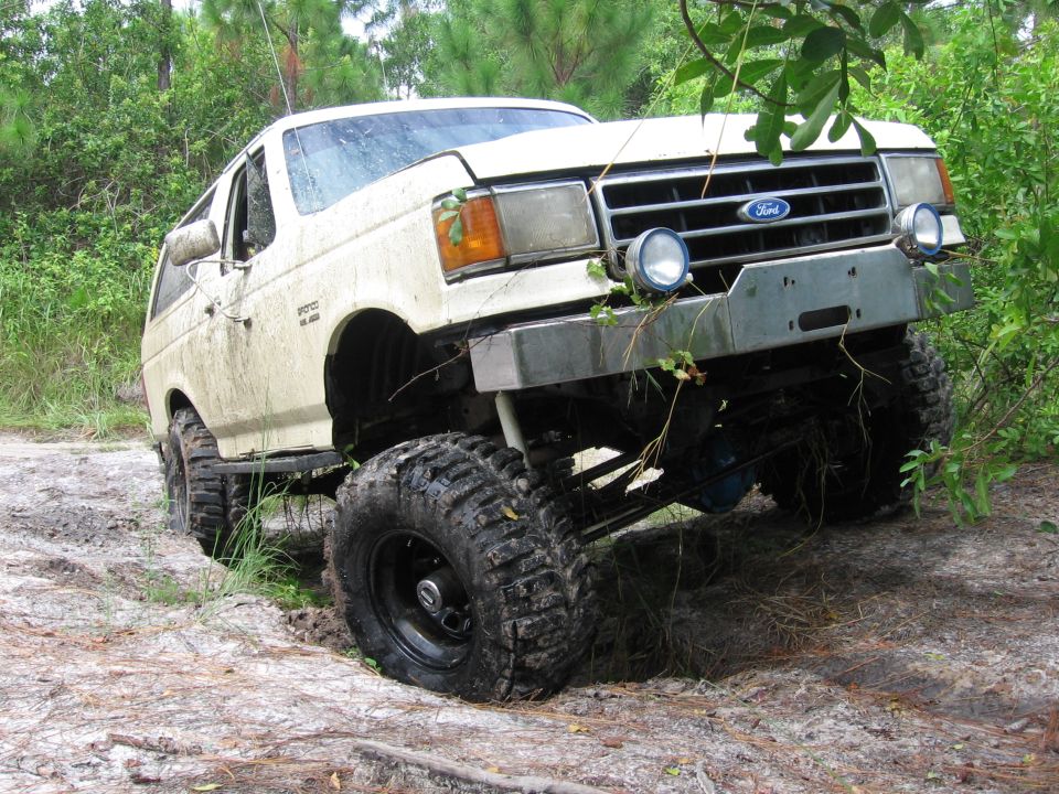 White Ford Bronco with off-road tires stuck in mud, front-left angle