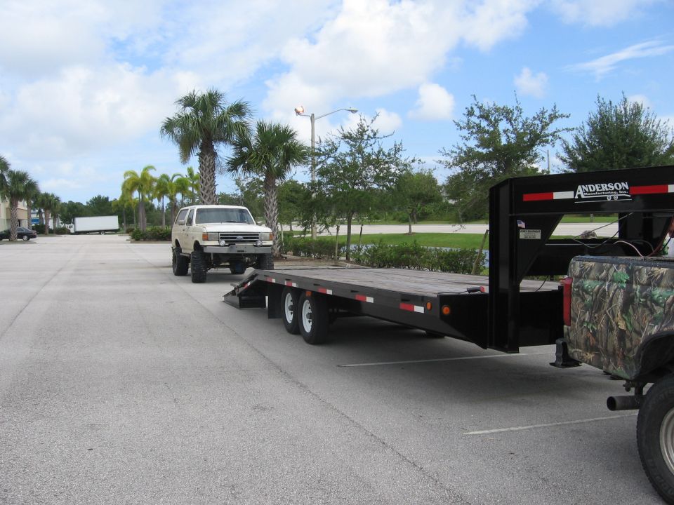 1989 Ford Bronco with lifted suspension and large tires, hitched to a black flatbed trailer