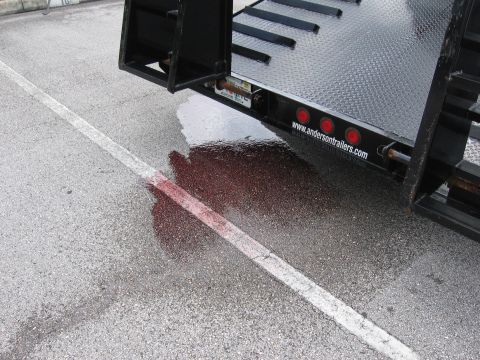 1989 Ford Bronco - A puddle of red fluid stains the asphalt near a trailer hitch, with a white line marking the parking space.