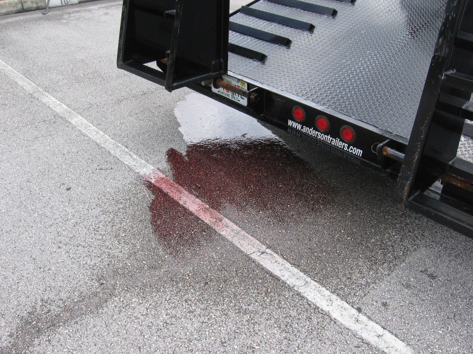 Trailer hitch with red fluid puddle on asphalt, white line, and www.andresontrailers.com text