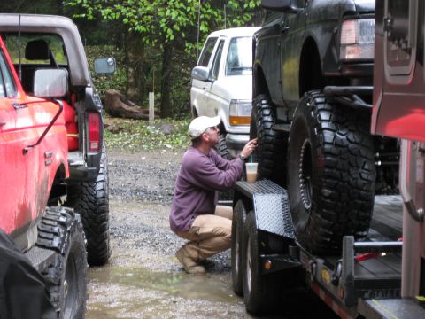 1979 Ford Bronco - A man pauses with a drink while standing next to several large off-road vehicles.