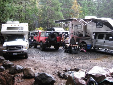 1979 Ford Bronco - A campsite scene with multiple vehicles including a red SUV and two RVs parked in a wooded area.