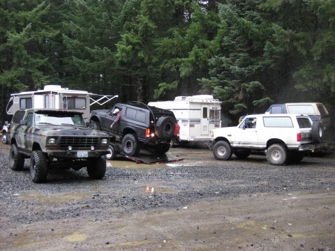 1979 Ford Bronco - Multiple Ford Broncos and RVs gathered in a muddy, wooded area.