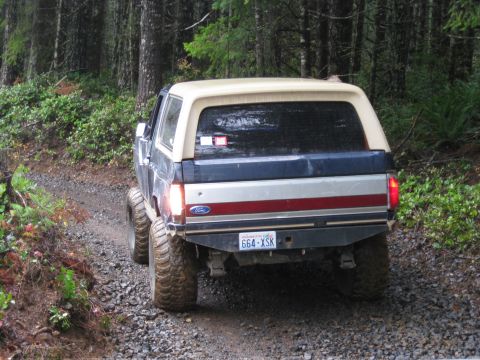 1979 Ford Bronco - A Ford Bronco drives on a gravel road through a forest.