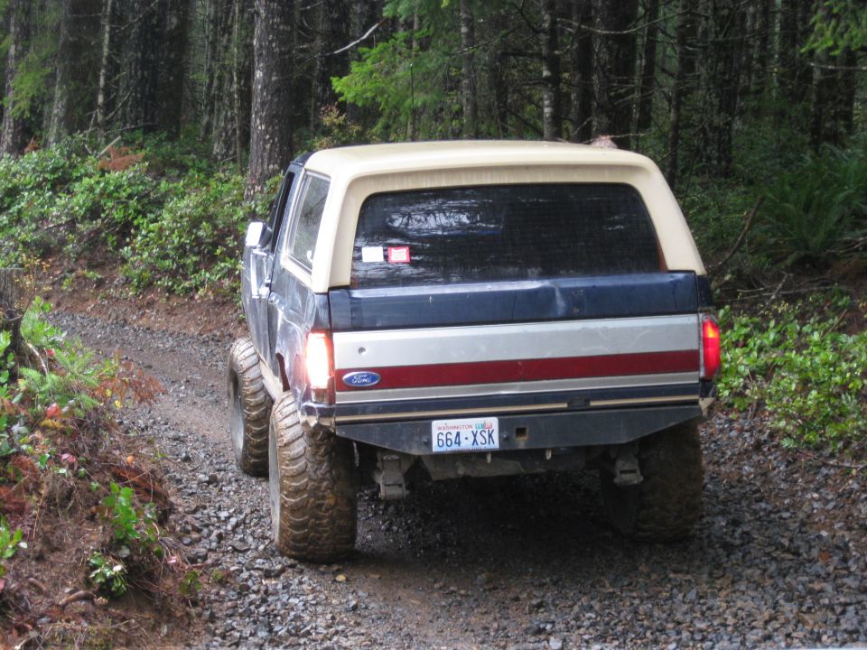 Dark blue and silver Ford Bronco with a tan top driving on a gravel road