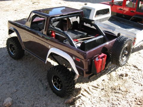 1988 Ford Bronco - A model Bronco with off-road modifications sits on sandy terrain next to other vehicles.