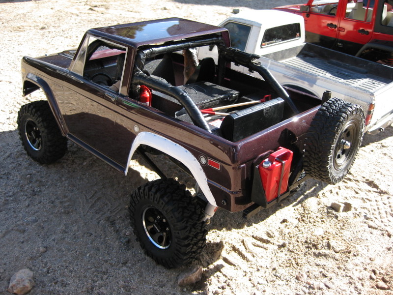 Model Bronco with roll cage, off-road tires, and jerry cans, viewed from the rear three-quarter angle