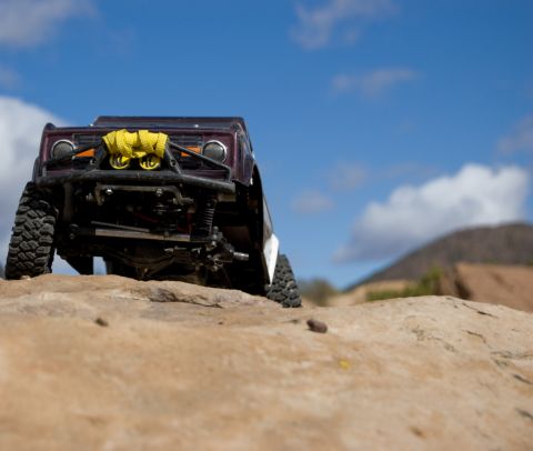 1988 Ford Bronco - RC rock crawler with custom bumper and tow straps sits on a rocky trail under a blue sky.