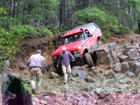 1979 Ford Bronco - A red SUV with a snorkel attachment navigates a challenging rocky trail with two people nearby.