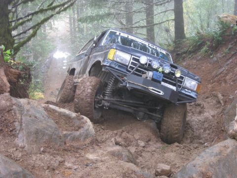 1979 Ford Bronco - This modified SUV tackles a challenging muddy off-road course, with a club sticker visible on its windshield.