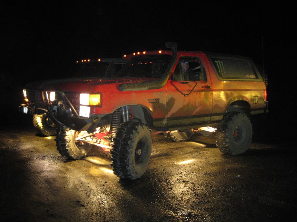 Red off-road SUV with large tires and lifted suspension, seen at night with headlights on