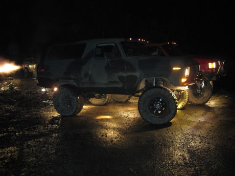1979 Ford Bronco - A lifted, camouflaged SUV with off-road tires is parked at night, with another vehicle visible behind it.