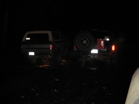 1979 Ford Bronco - Two SUVs are parked at night, one with a spare tire and gas can on the back.